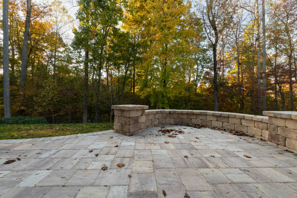 Picturesque backyard view in autumn season with patio pavers and stone wall, autumn leaves, and colorful woods in the background.